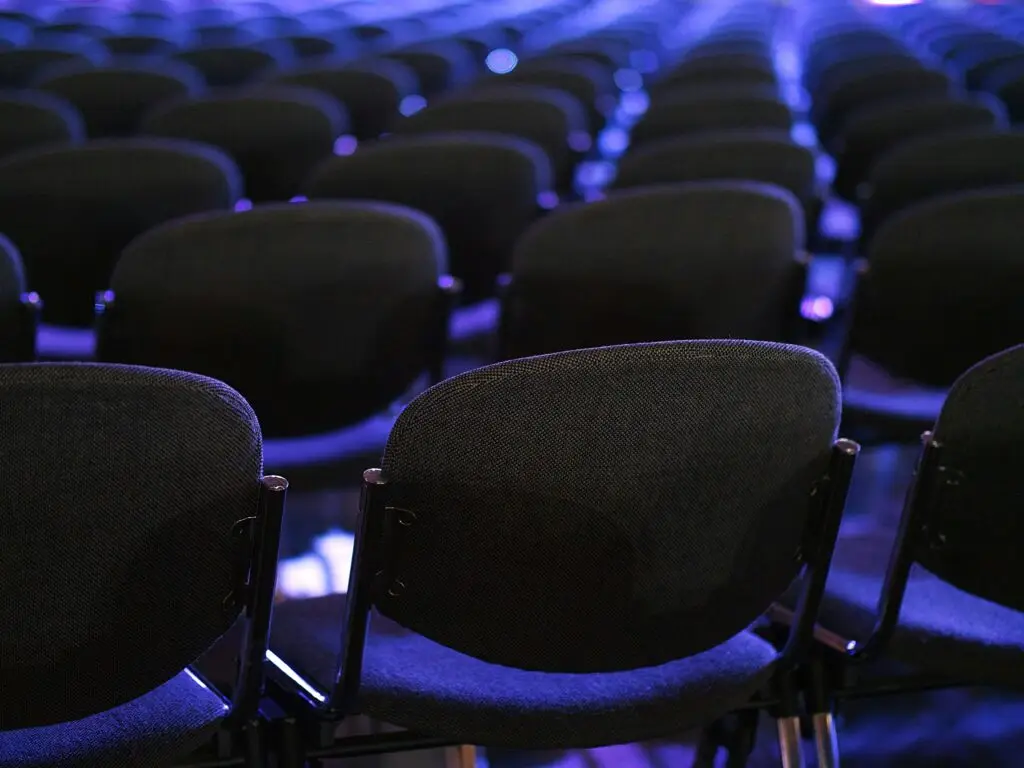 Organisation von Anlässen Stuhlreihen in einem Saal mit blauem Licht Atmosphäre alles bereit kurz vor einem Event Foto von Andrei Stratu auf Unsplash