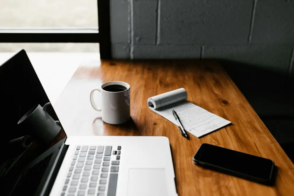 iMac Kaffeetasse Notizbuch und Smartphone liegen bereit auf Arbeitsplatz für Online-Recherchen Foto von Andrew Neel auf Unsplash