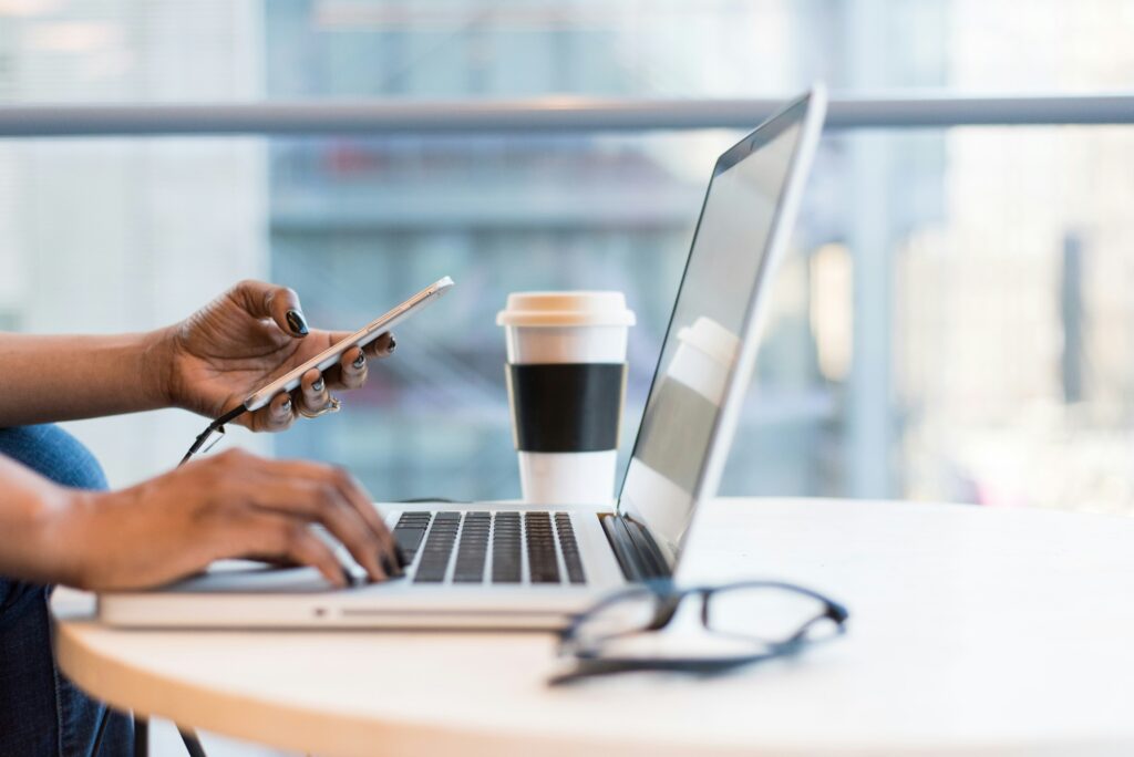Virtuelle Assistenz Dienstleistungen Person benutzt Smartphone und iMac Kaffeebecher und Brille neben iMac von Christina @ wocintechchat.com auf unsplash