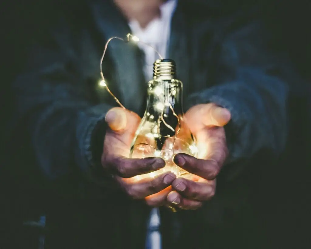 Virtuelle Assistenz Preise Mann in Businessanzug hält eine Glühbirne mit Weihnachtsbeleuchtung in Vordergrund -Riccardo Annandale auf Unsplash