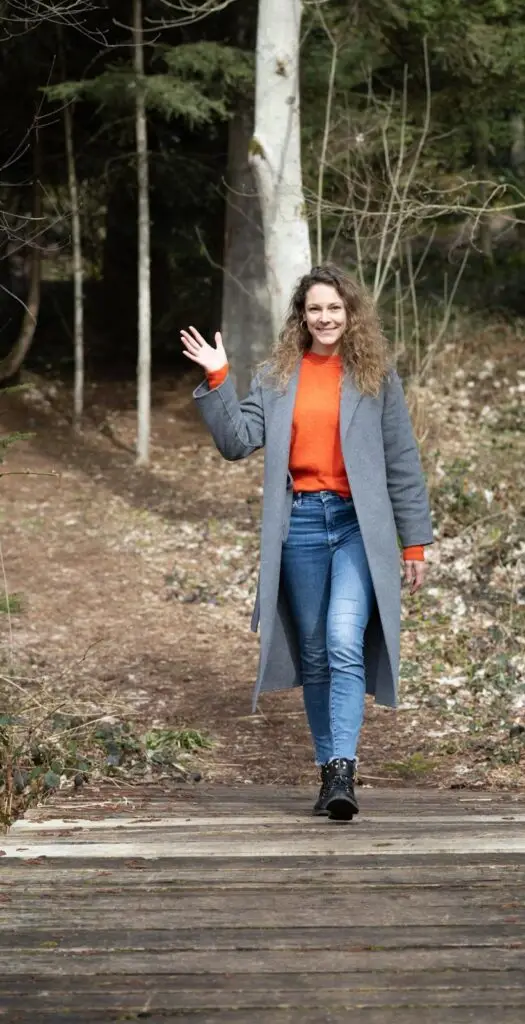 Francesca Schori im Wald schaut direkt in Kamera und winkt glücklich