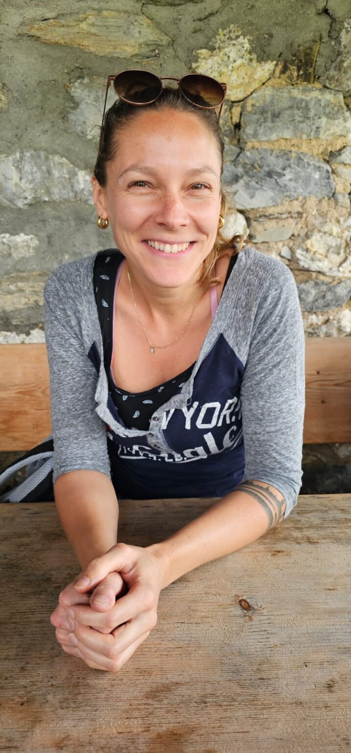 Francesca Schori lacht an Holztisch sitzend in die Kamera