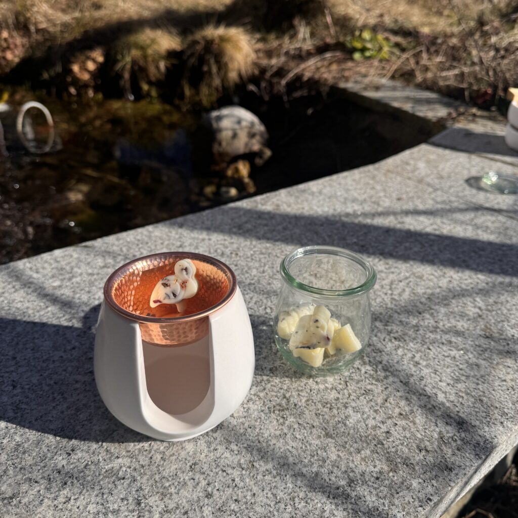 Duftlampe mit einer Kupferschale und einem Duftwachs in der Schale, daneben ein Glas mit weiteren Duftwachsen